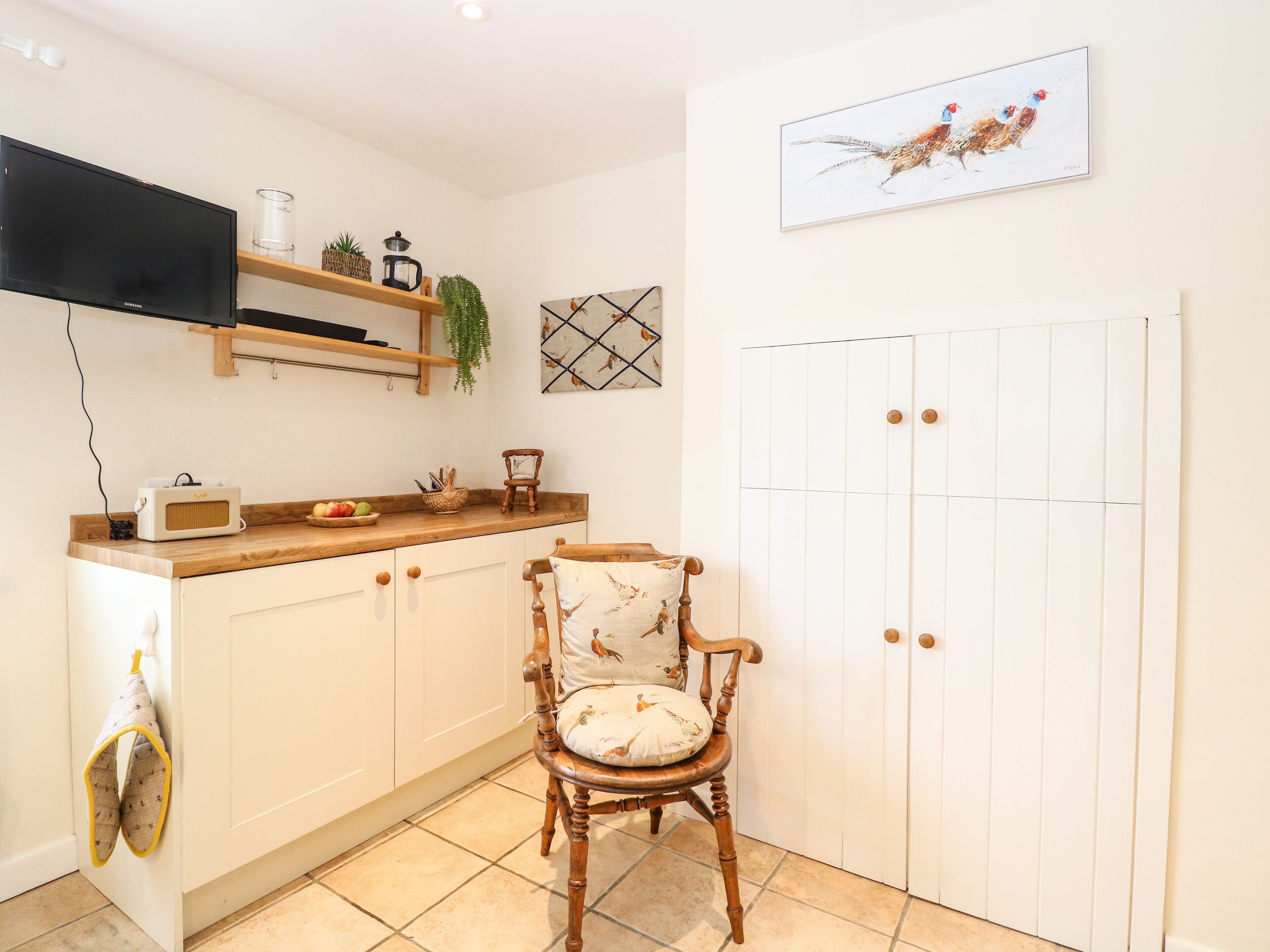 A kitchen with a wooden countertop, a chair with a cushion, a television, and a door with a panel.