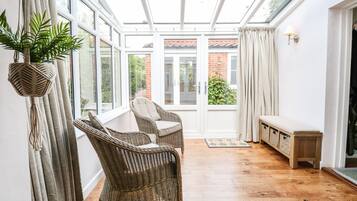 A sunlit room with wicker furniture, a bench, and a view through a glass door to a brick building.
