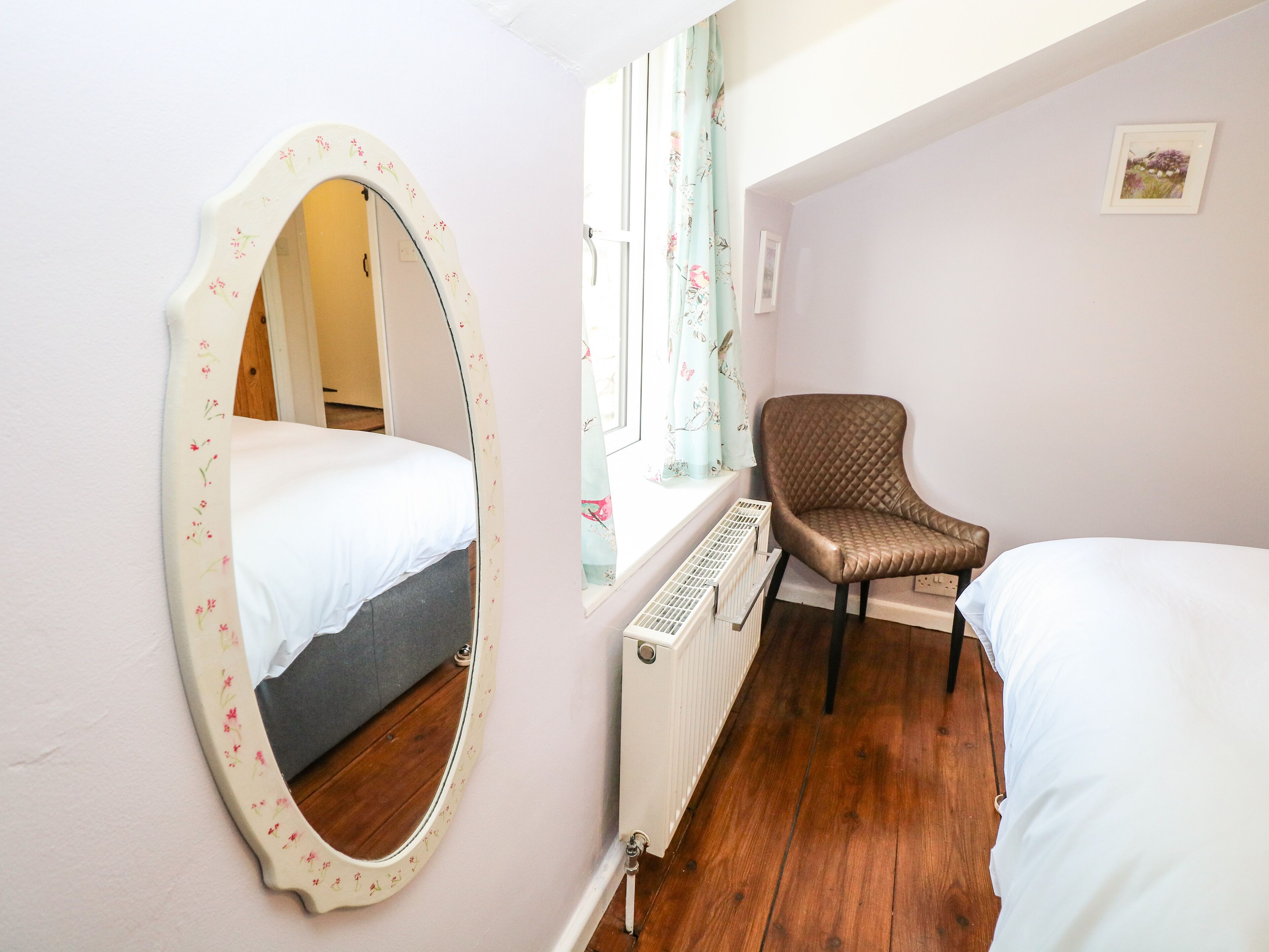 A bedroom with a bed, a chair, a radiator, and a window with floral curtains.