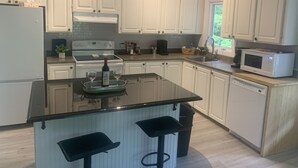 Eine moderne Küche mit weißen Schränken, einer zentralen Kochinsel mit Barhocker, einem eingebauten Backofen und einer Mikrowelle.
