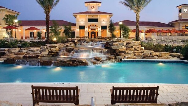 Ein Hotel mit Pool, Wasserfall, Palmen und Sitzbereichen im Freien.