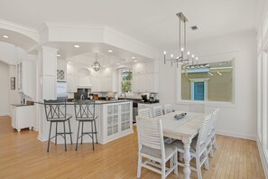 Une cuisine spacieuse avec des meubles blancs, un îlot central doté de tabourets de bar et un coin repas avec une table et des chaises blanches.