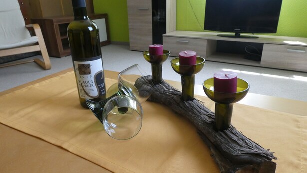 Una bottiglia di vino, un bicchiere e tre candele su un tavolo di legno.