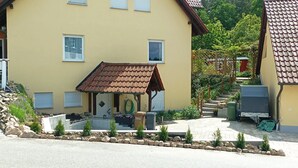 Una casa a due piani con un piccolo patio, una zona salotto all'aperto coperta e un vialetto in pietra che conduce all'ingresso.
