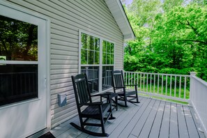 Relax on the porch with two comfortable chairs and a small table, surrounded by lush greenery.