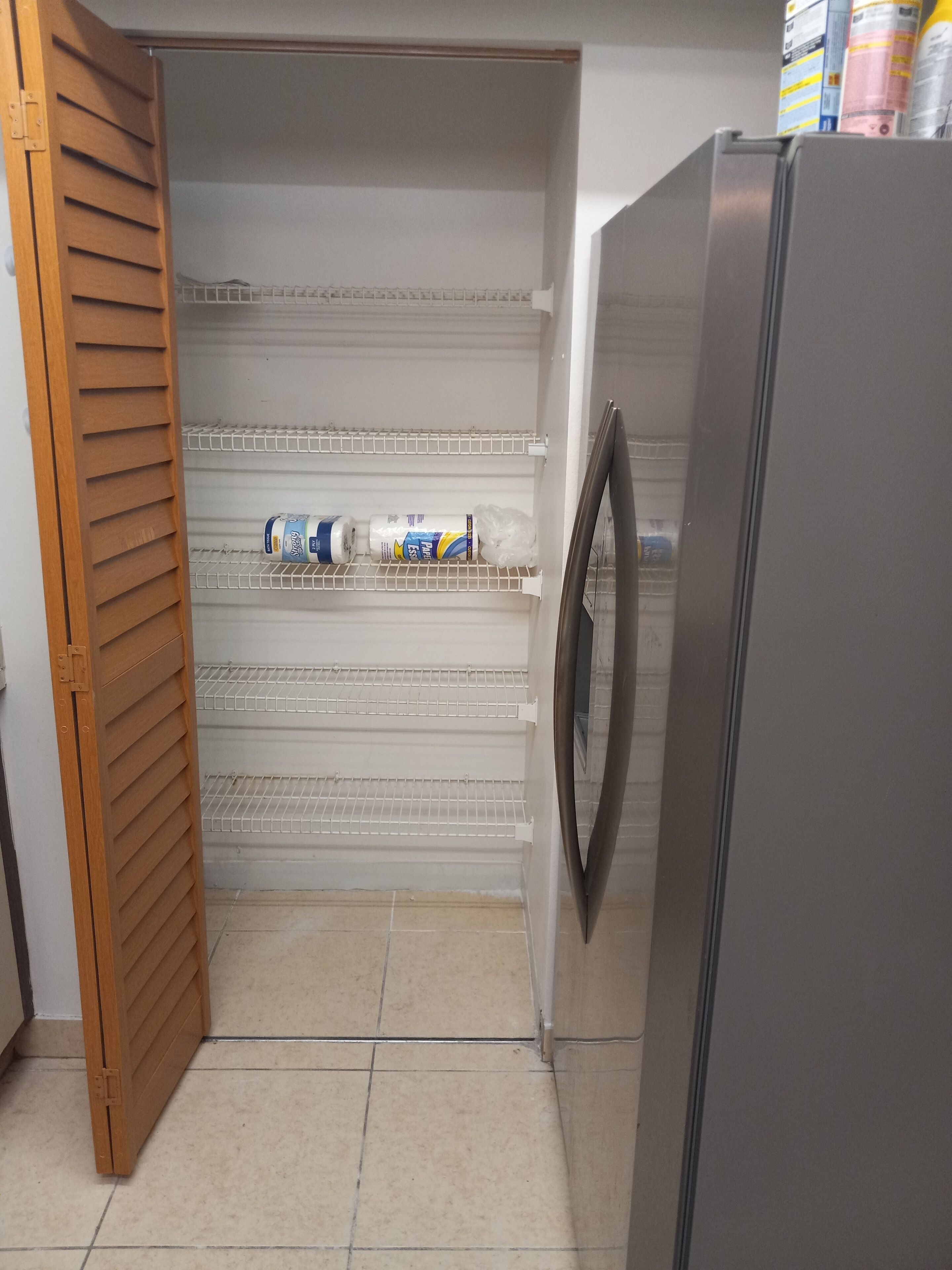 Una cocina con un refrigerador, una puerta de madera y un estante con algunos objetos.