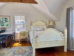 Un dormitorio con cama, lámparas de noche, un escritorio con silla, una cafetera y una ventana.