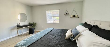A bedroom with a bed, bedside table, mirror, window, and two wall-mounted shelves.