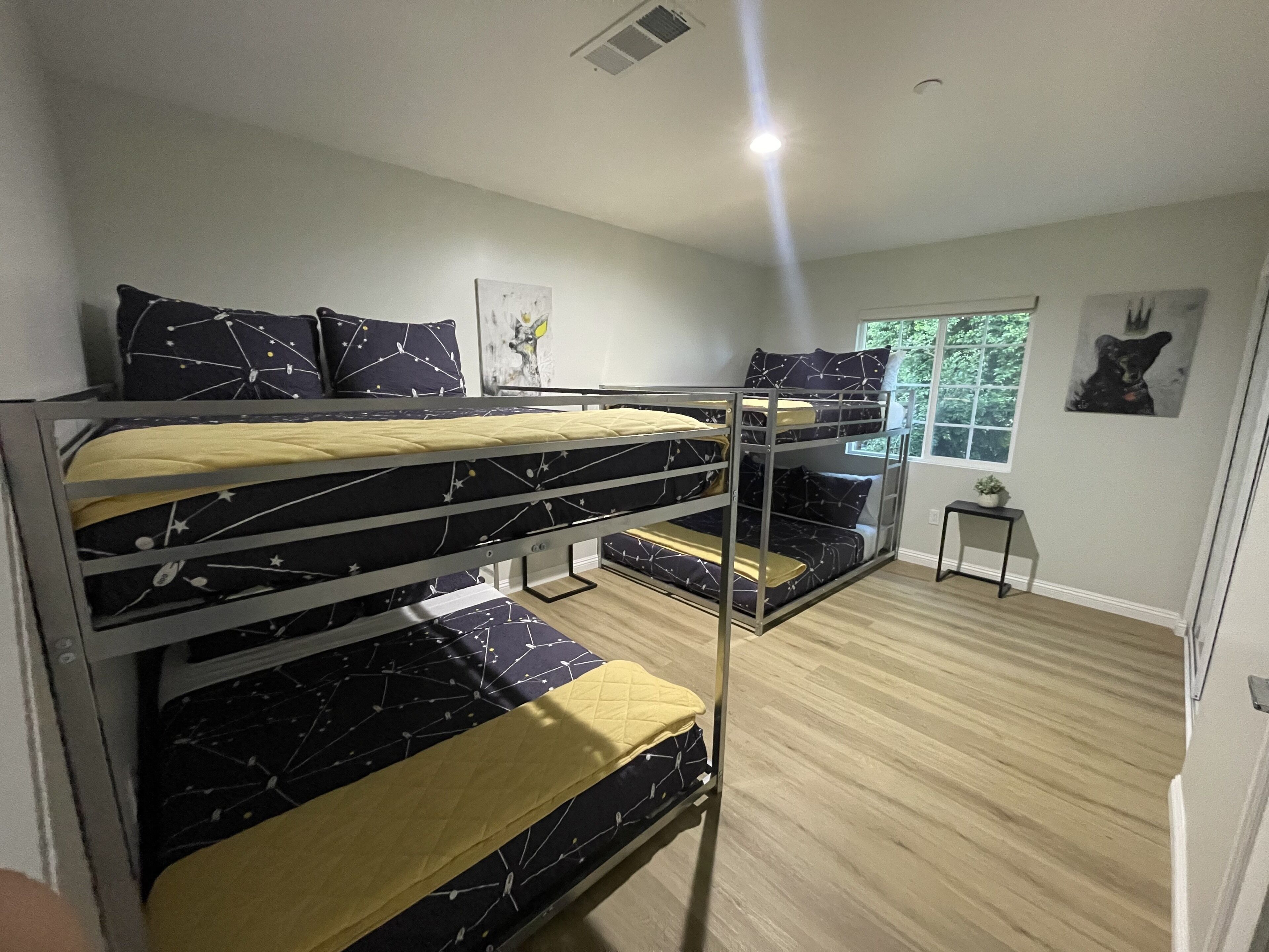 A bunk bed room with a window, a small table, and a picture on the wall.