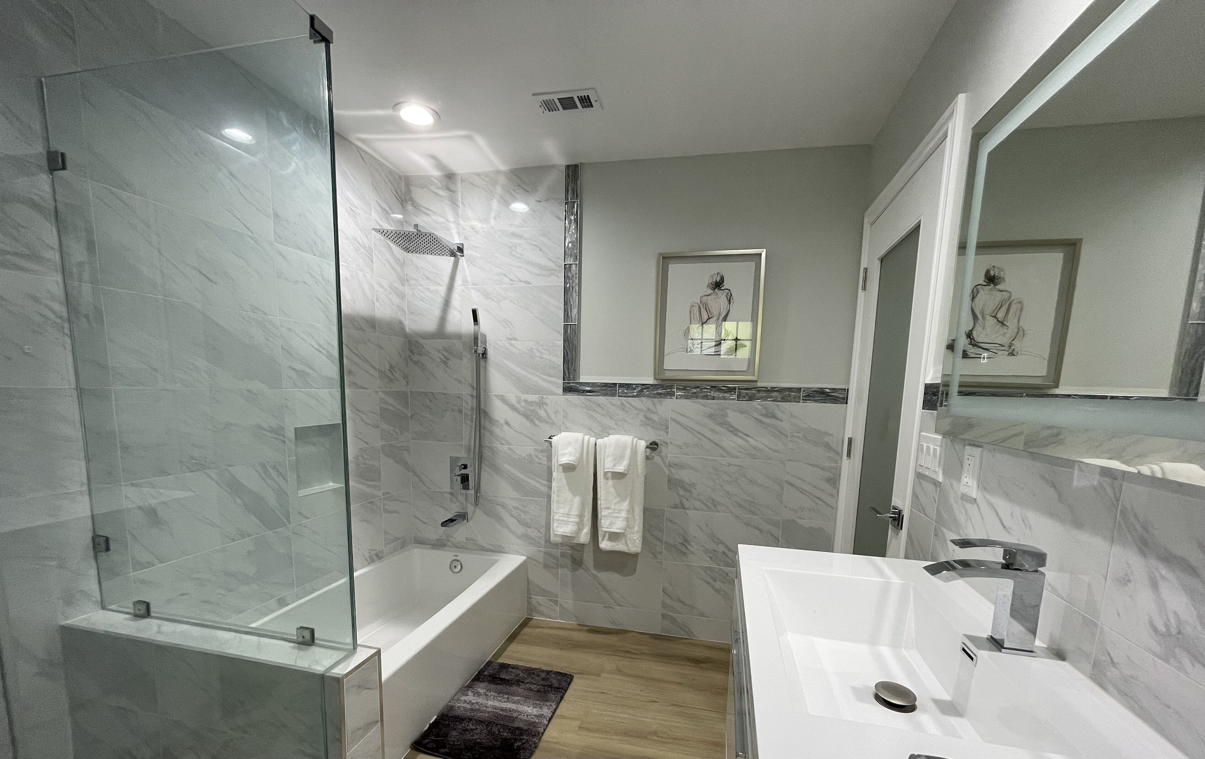 A modern bathroom with a glass-enclosed shower, a bathtub, and a vanity with a mirror.