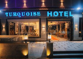 The exterior of the Turquoise Hotel with illuminated signage, large windows, and outdoor seating area.