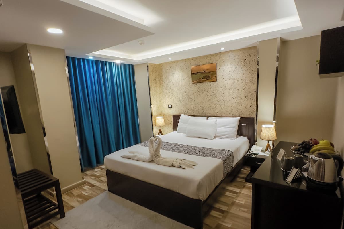 A modern hotel room with a large bed, a desk with a telephone, and a flat-screen TV.