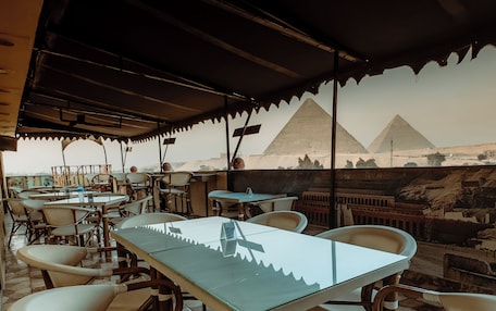 An outdoor dining area with tables and chairs, a view of the pyramids, and a tiled floor.