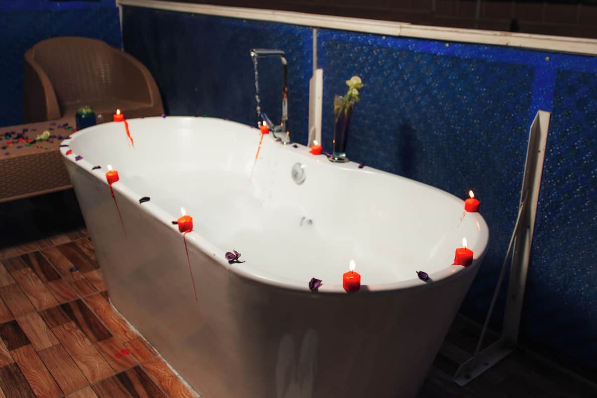 A bathtub with candles on a wooden floor, a chair, and a blue wall with a hanging towel.