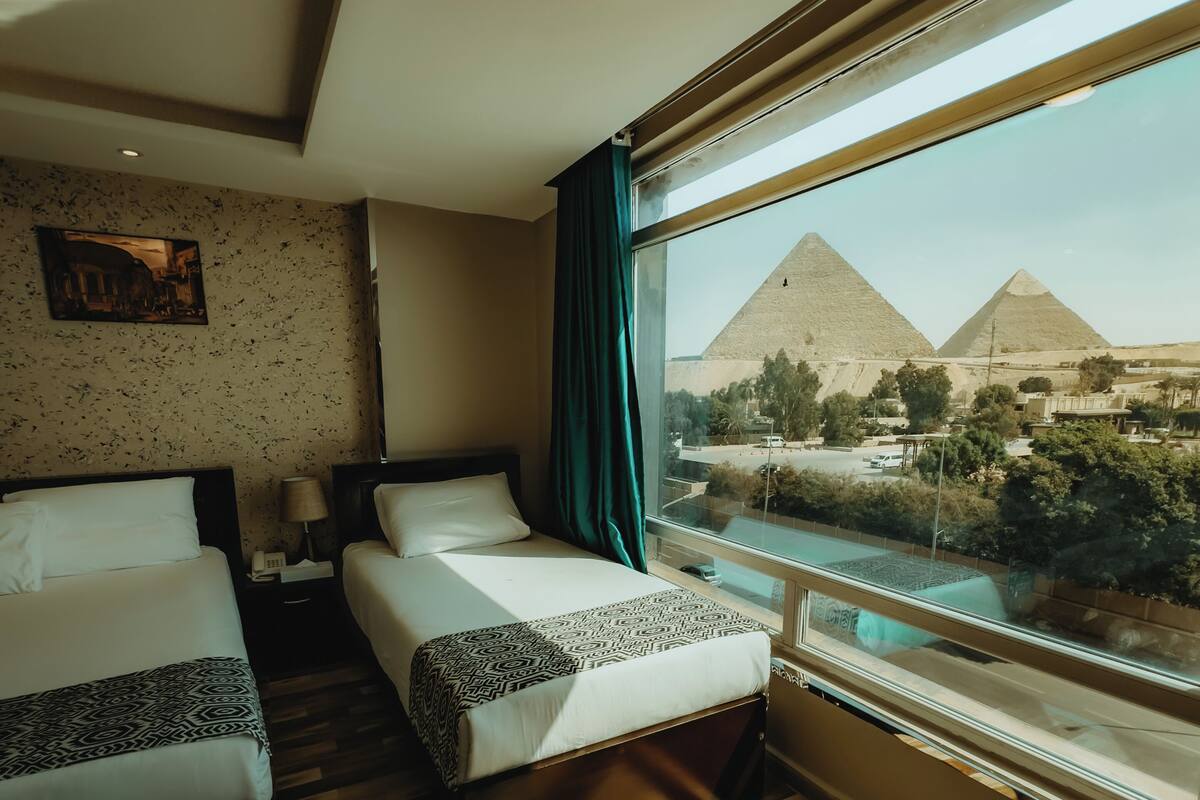 A hotel room with two beds, a view of the pyramids, and a wooden floor.