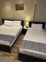Deux lits doubles avec du linge de lit blanc, une table de chevet avec une lampe, un tableau au mur et un tapis à motifs.
