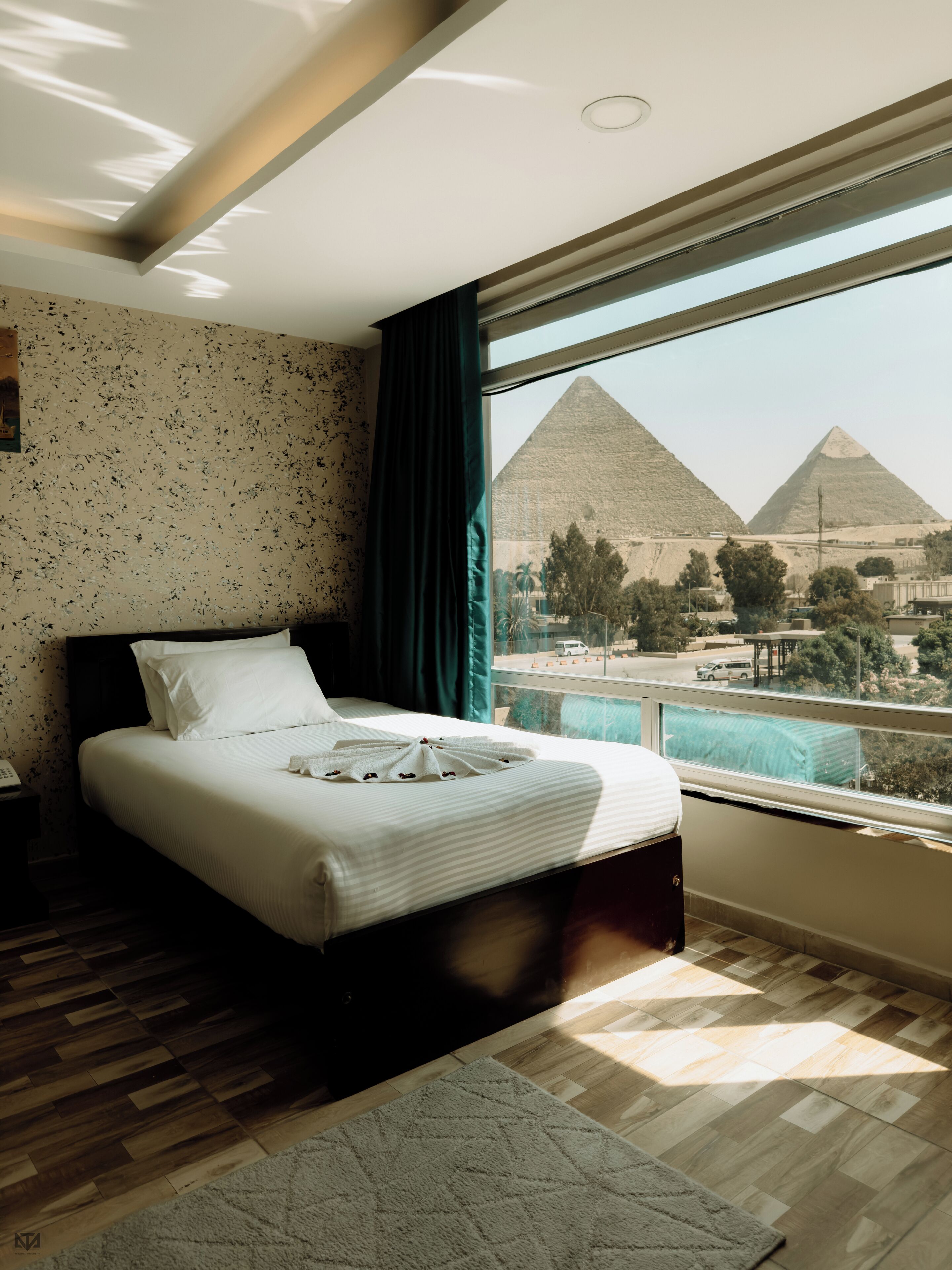 Habitación de hotel con una cama grande, vista a las pirámides y piso de madera.