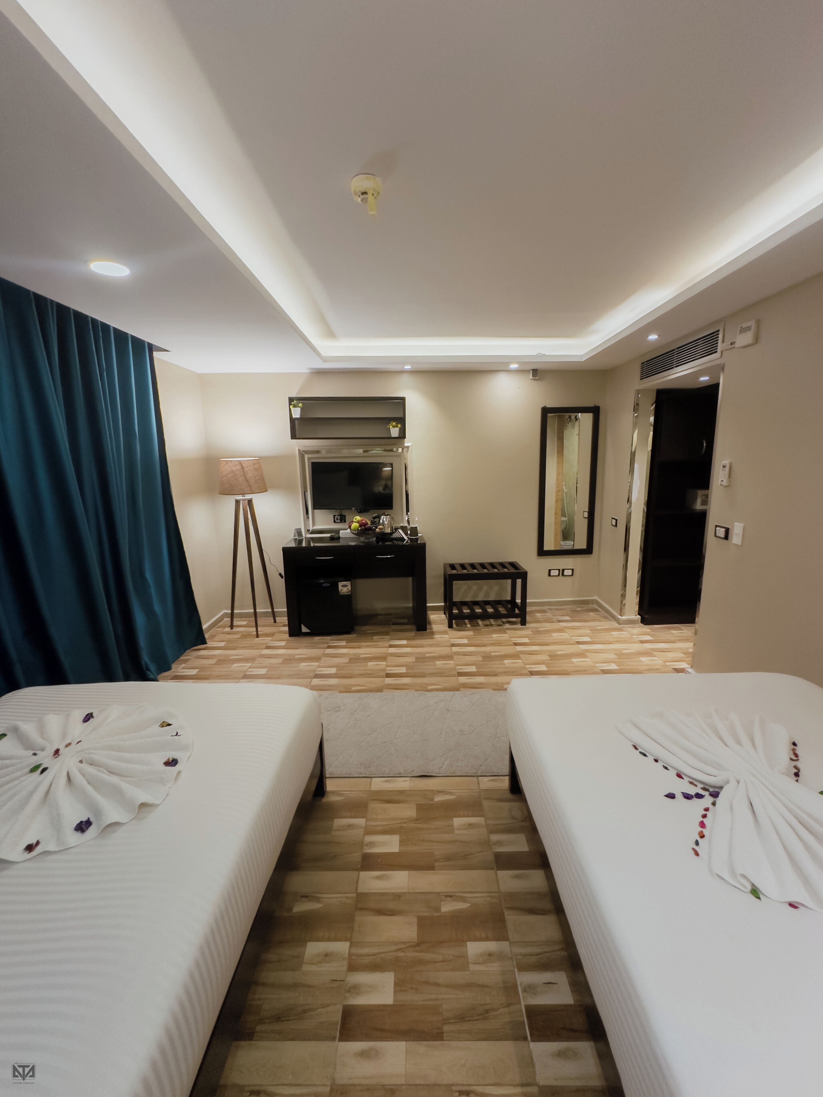 Habitación de hotel con dos camas, un escritorio, un espejo y una lámpara del techo.