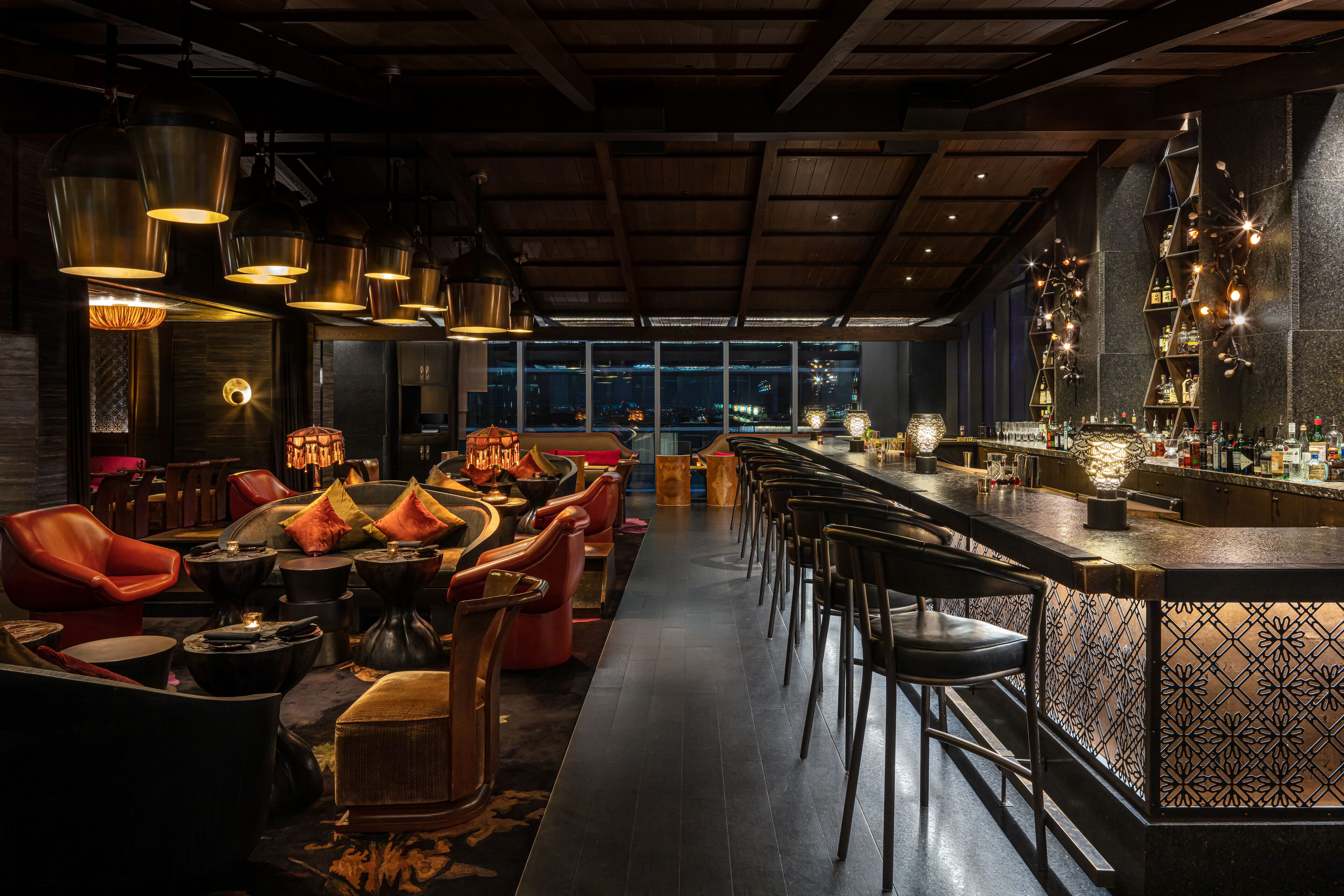 Uma área de bar moderna com pé-direito alto, vigas aparentes e um balcão comprido com banquetas.