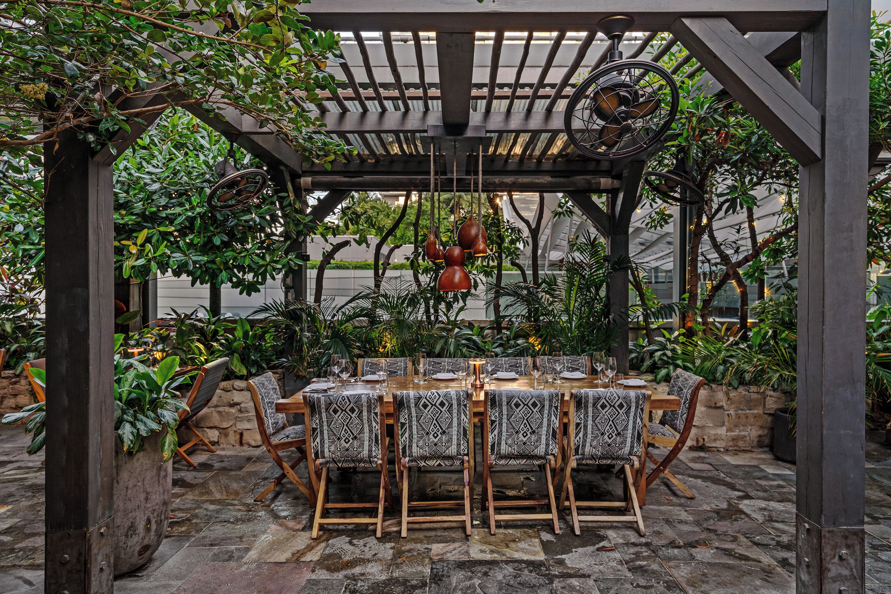 An outdoor dining area with a pergola, wooden chairs, and a table set for four.