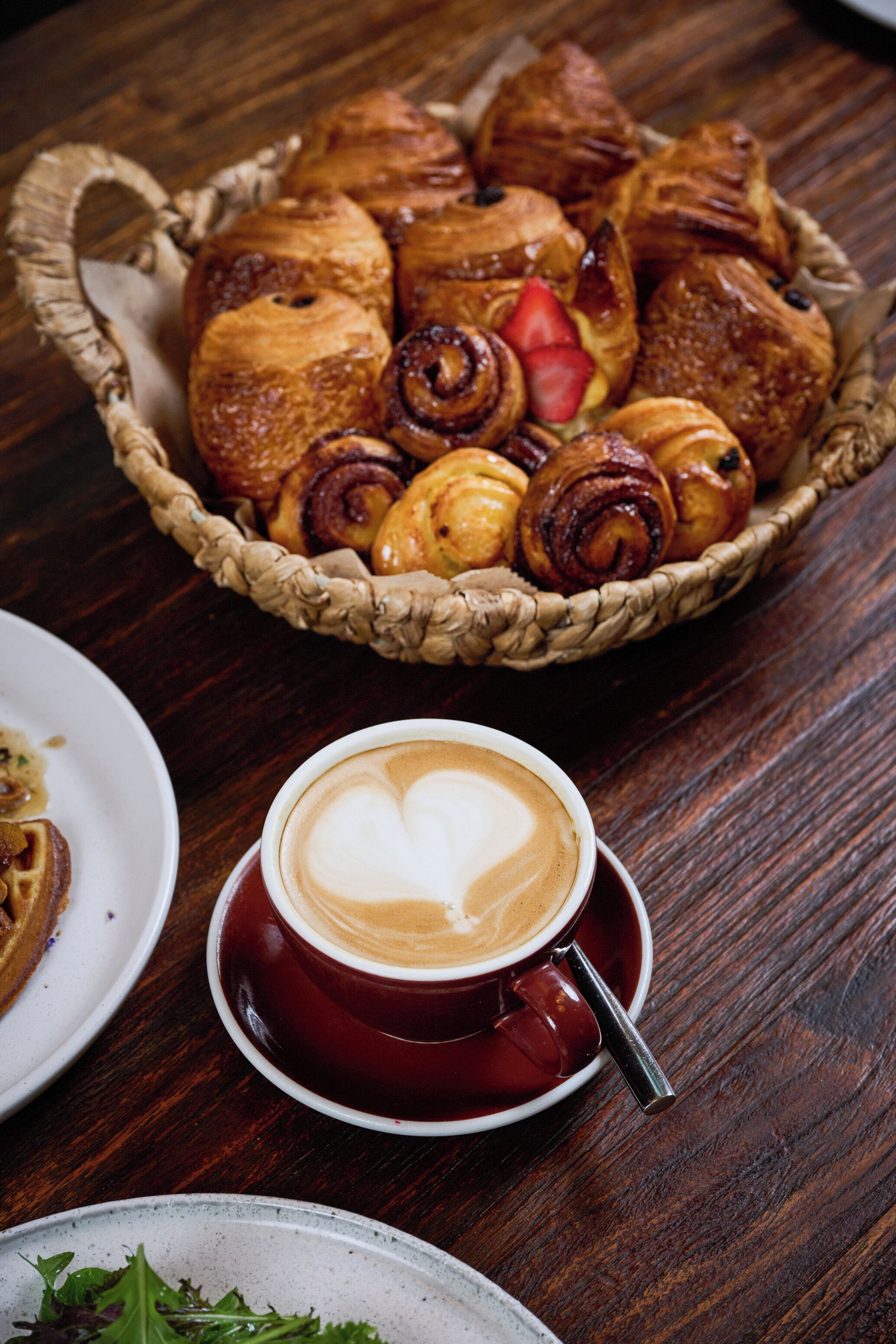 Una cesta de pasteles y una taza de café con un dibujo de corazón hecho en espuma.