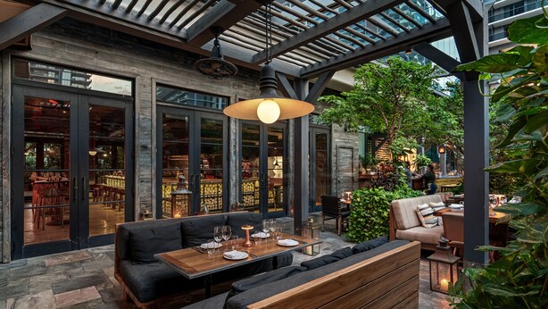 Un espace de restauration en plein air avec une table en bois prévue pour quatre personnes, entourée de sièges noirs rembourrés.