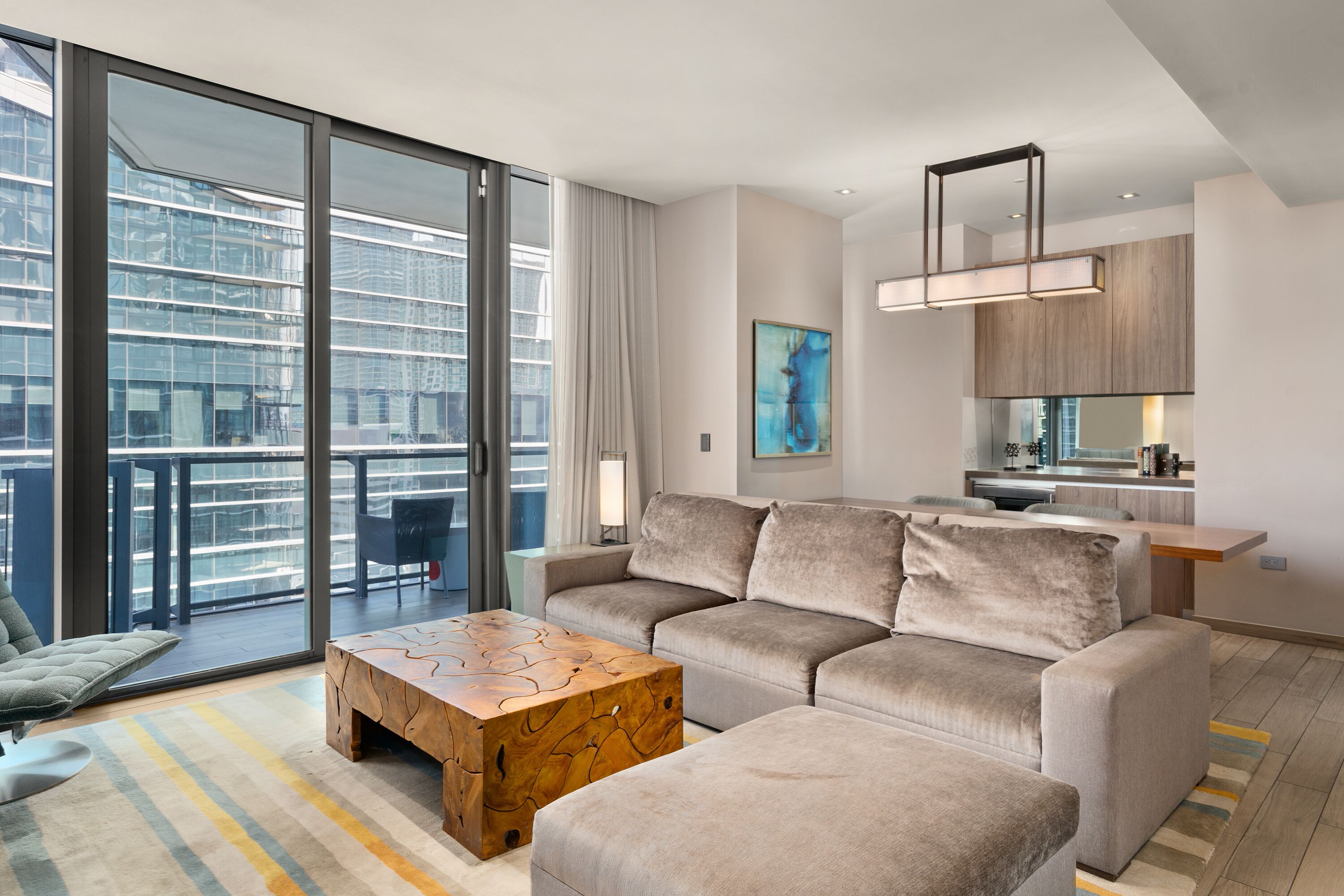 Ein modernes Wohnzimmer mit Sofa, Hocker und Couchtisch, einem Essbereich und einer Küche mit großem Fenster.