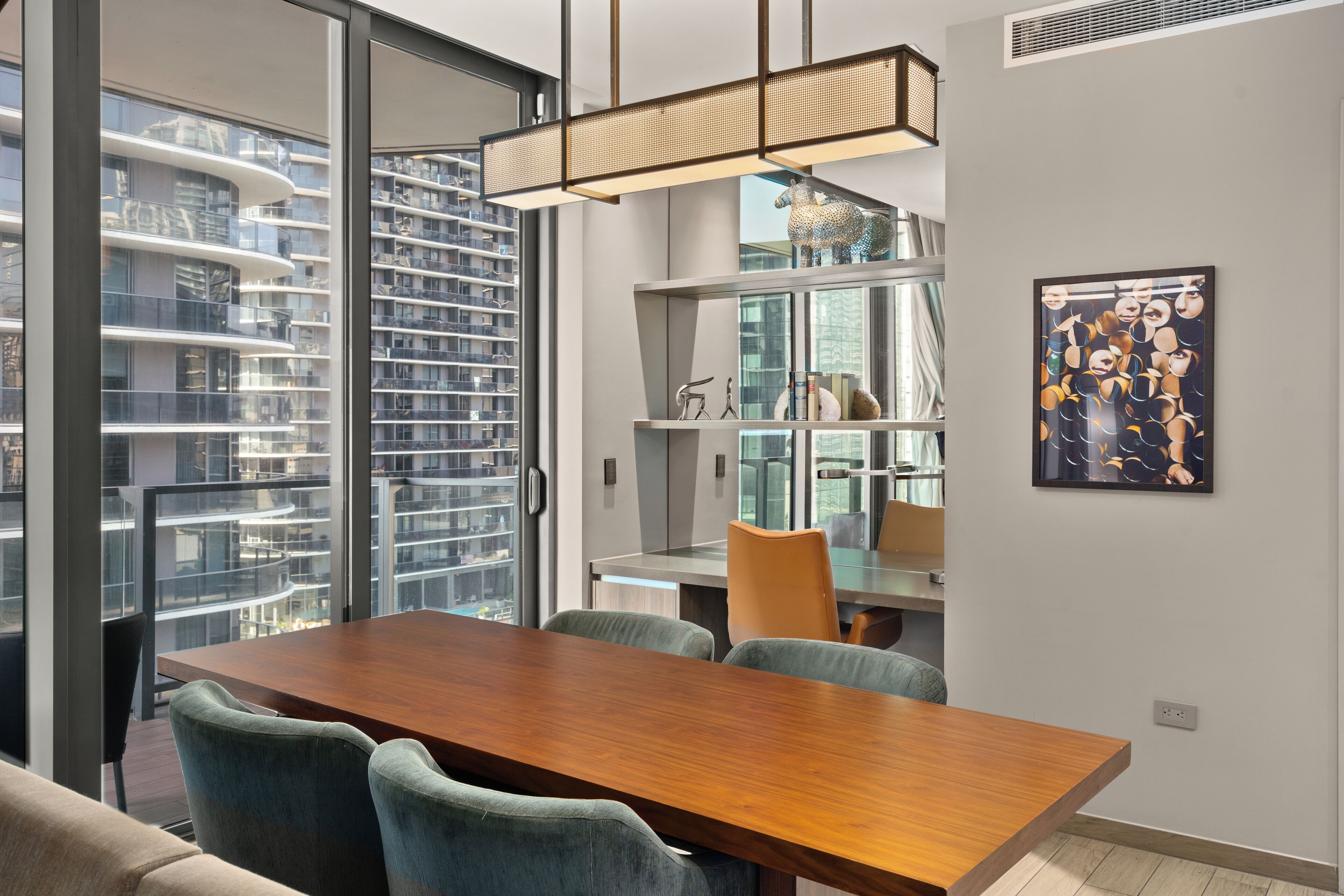 Un comedor moderno con una mesa y sillas de madera, un panel de vidrio y vistas a la ciudad a través de amplios ventanales.