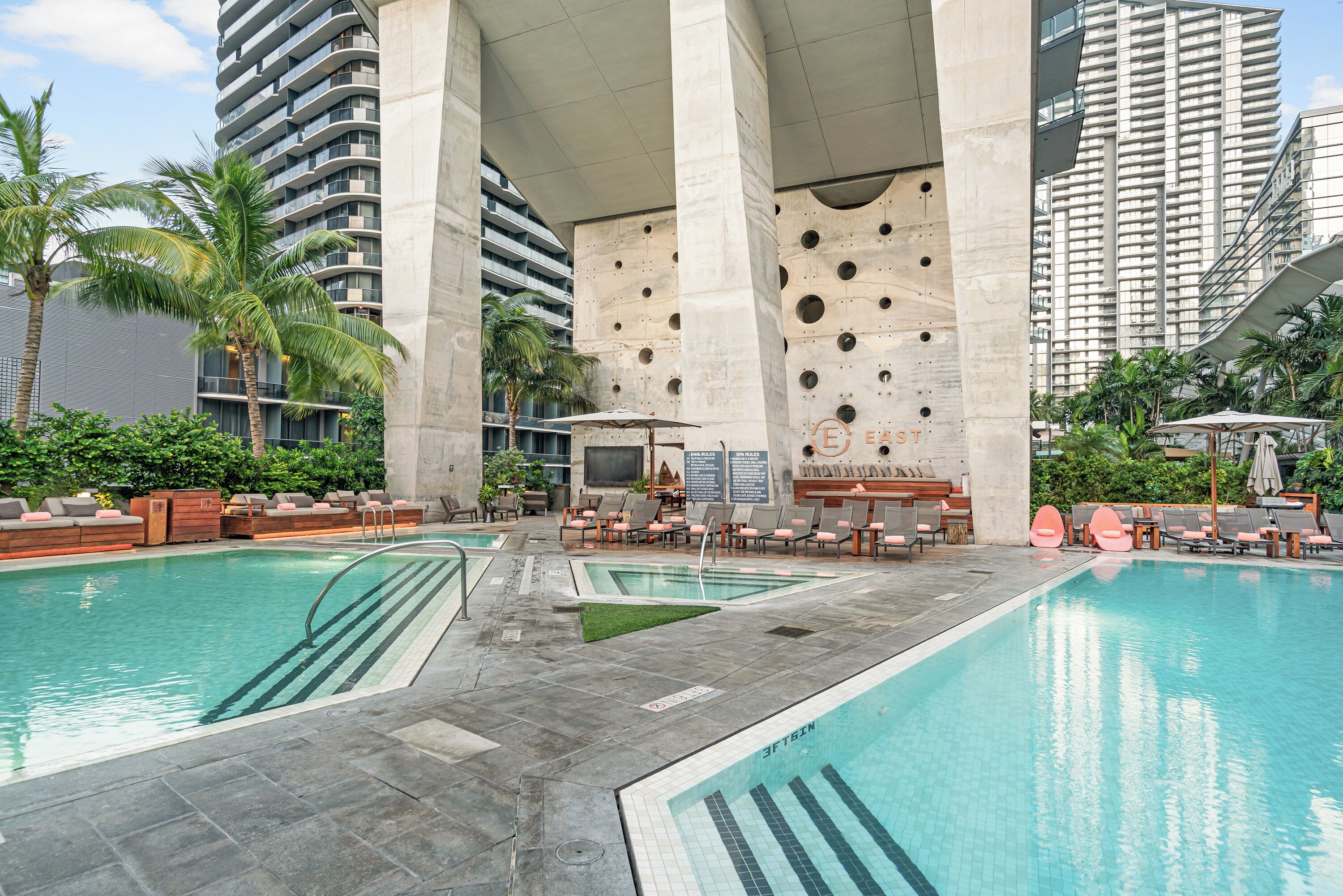 A pool area with lounge chairs and a seating area, surrounded by tall buildings and palm trees.
