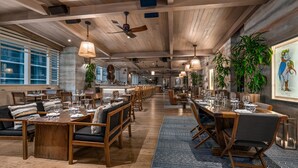 Un restaurant spacieux avec des tables et des chaises en bois, de grandes fenêtres et des plantes suspendues.
