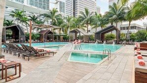 Un espace piscine sur le toit, comprenant plusieurs piscines, des chaises longues et des parasols.