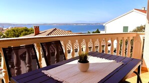 Enjoy the breathtaking sea and mountain views from this balcony with a table, chairs, and a potted plant.