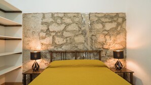 Una habitación con pared de piedra, una cama con colcha amarilla y dos lámparas de noche.