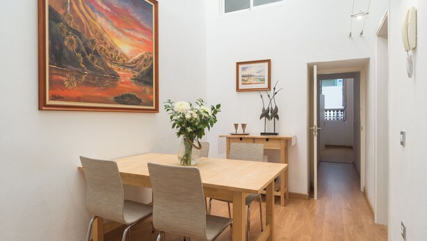 Un comedor con una mesa y sillas de madera, un jarrón de flores y dos cuadros en la pared.