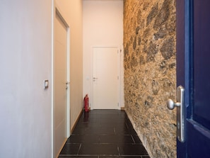 A hallway with a white door at the end, a fire extinguisher on the floor, and a stone wall on one side.