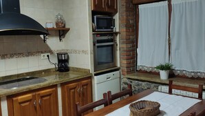 A kitchen with wooden cabinets, a stove, a microwave, and a dishwasher. There is a dining table with chairs and a window with curtains.