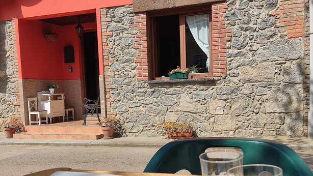 A table with sandwiches and drinks, a stone building with a red wall and a window, and a bench outside.