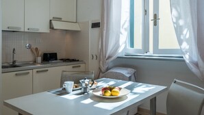 Cucina con mobili bianchi, lavello e finestra con tende leggere.
