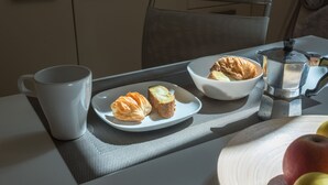Una tavola imbandita per la colazione con croissant, una caffettiera e una ciotola di frutta.