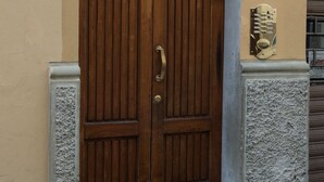 Una porta in legno a due battenti con maniglia in metallo, una targa con un numero e una piccola placca decorativa al muro.