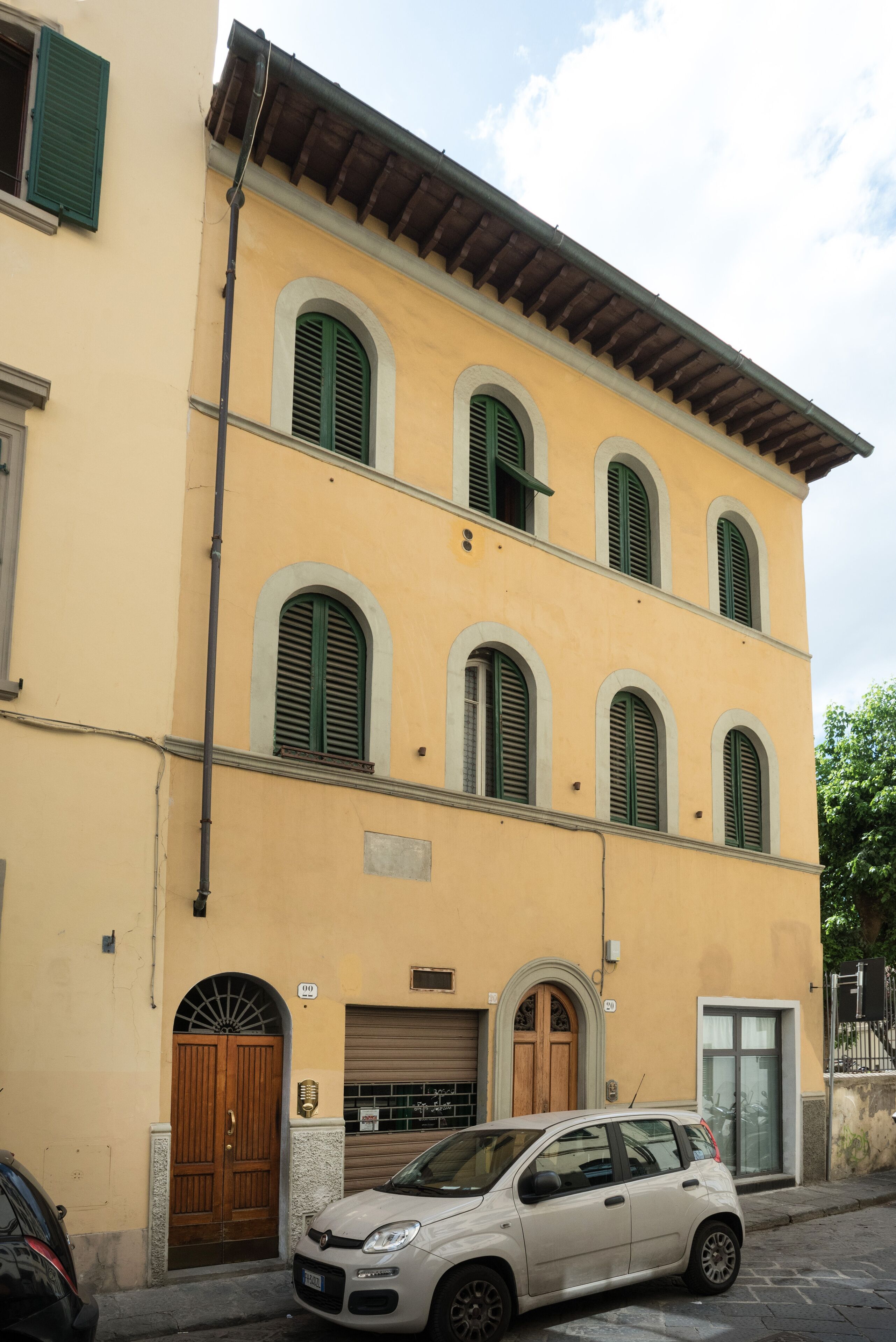A two-story building with a yellow facade, green shutters, and a wooden door.