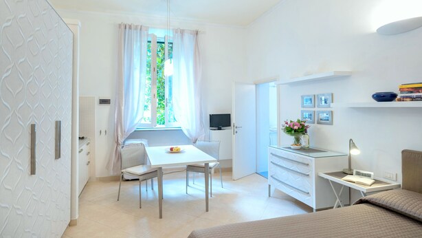 Una camera d'albergo moderna con un letto, una scrivania, una sedia, una TV e una finestra con tende.