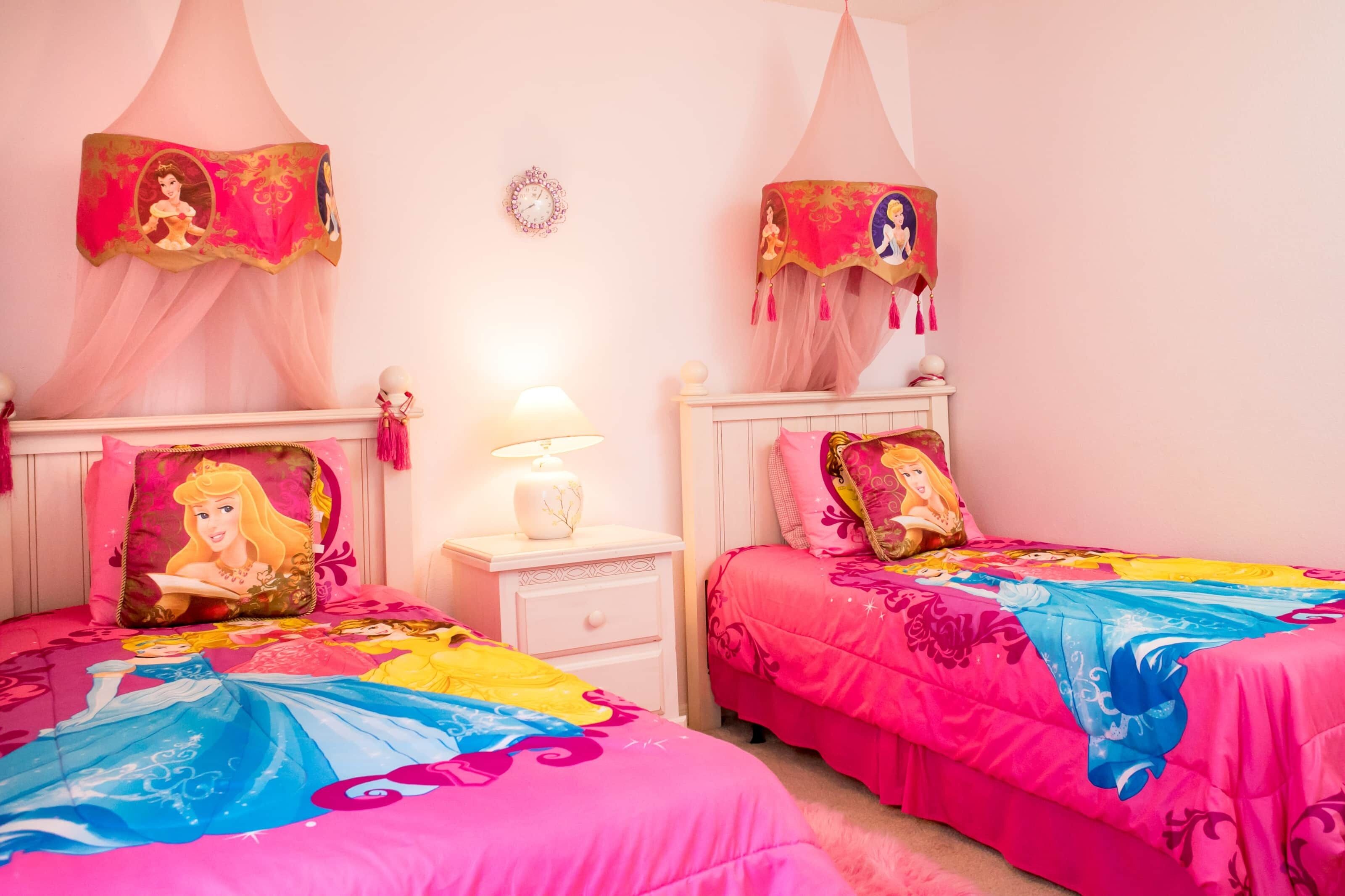 A bedroom with two beds, each with a canopy and themed bedding. There is a nightstand with a lamp between the beds.