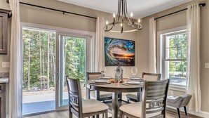 A dining area with a round table set for four, surrounded by chairs, a chandelier, and a painting above the table. - Shipbuilder’s Retreat sleeps 6, 5 minutes to Harbor (East Boothbay)