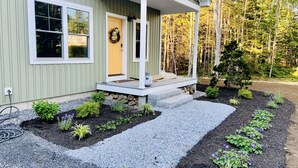 A house with a porch, a front door, and a garden with plants and a gravel path. - Shipbuilder’s Retreat sleeps 6, 5 minutes to Harbor (East Boothbay)