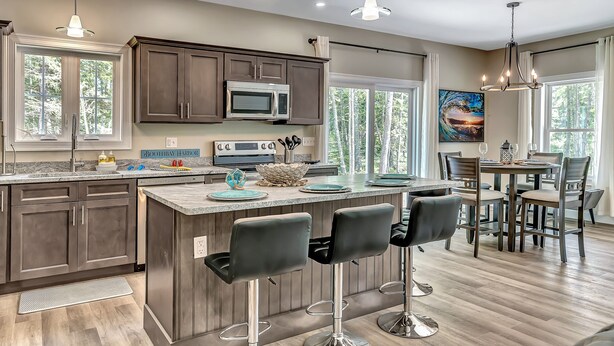 A modern kitchen with dark cabinets, a central island with bar stools, and a dining area with a round table and chairs. - Shipbuilder’s Retreat sleeps 6, 5 minutes to Harbor (East Boothbay)