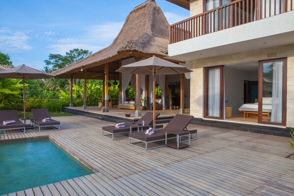 A poolside area with lounge chairs and umbrellas, a thatched-roof structure, and a modern building with large windows. - Villa Lumia - 4BR · 20m Pool · Jacuzzi · Private Chef · Rice Fields · Ubud (Ubud)