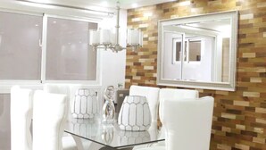 Un comedor moderno con una mesa de vidrio rodeada de sillas blancas, una pared de madera con un diseño de mosaico y un espejo grande sobre la mesa.