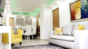 Una sala moderna con un sofá blanco, un sillón amarillo y una zona de comedor al fondo.