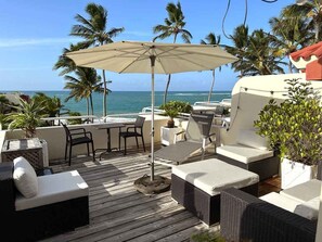 A deck with outdoor seating, including sofas and chairs, a table, and an umbrella. - Nanny Estates, Cabarete Beach House A5 (Cabarete)